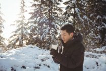 Человек в теплой одежде держит чашку кофе в течение зимы — стоковое фото