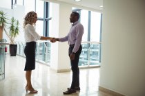 Business executives shaking hands at office corridor — Stock Photo