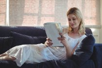 Красива жінка сидить на дивані і читає журнал у вітальні вдома — стокове фото