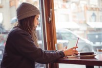 Женщина в зимней одежде с помощью цифрового планшета в ресторане — стоковое фото