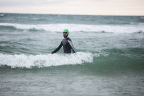 Male athlete in wet suit standing in sea — Stock Photo