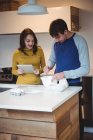 Пара с помощью цифрового планшета во время подготовки печенье на кухне дома — стоковое фото