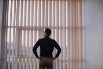 Rear view of man standing with hands on hips near window blinds — Stock Photo