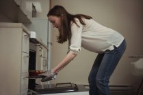 Mujer quitando pastel horneado del horno en la cocina en casa - foto de stock