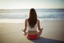 Rückansicht einer Frau, die am Strand Yoga macht — Stockfoto