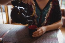 Partie médiane de la femme versant le thé dans la tasse dans le restaurant — Photo de stock