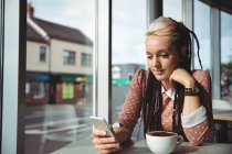 Mulher usando telefone celular enquanto toma café no café — Fotografia de Stock