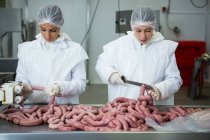 Carniceiros fêmeas cortando salsichas na fábrica de carne — Fotografia de Stock