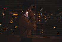 Чоловік дивиться крізь вікно під час розмови на мобільному телефоні вночі — стокове фото