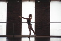 Ballerina practicing ballet move at barre in ballet studio — Stock Photo