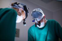 Cirujanos que usan lupas quirúrgicas mientras realizan operaciones en quirófano - foto de stock
