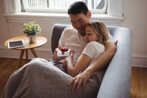 Man giving surprise gift to his woman on sofa at home — Stock Photo