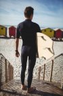 Vista posteriore del surfista in piedi con tavola da surf sulla spiaggia — Foto stock
