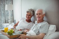 Senior couple holding breakfast on bed in bed room — Stock Photo