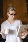 Mujer usando tableta digital mientras toma café en la cocina en casa - foto de stock