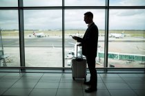 Homme d'affaires avec bagages utilisant un téléphone portable à l'aéroport — Photo de stock