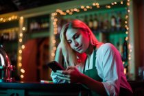 Garçonete usando seu telefone celular no balcão do bar — Fotografia de Stock