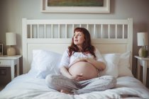 Femme enceinte réfléchie se détendre sur le lit dans la chambre — Photo de stock