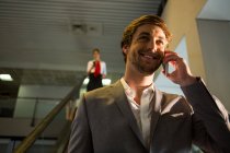 Бизнесмен на эскалаторе разговаривает по мобильному телефону в аэропорту — стоковое фото