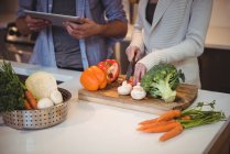 Sección media de la pareja que usa tableta digital mientras corta verduras en la cocina - foto de stock