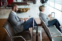 Uomini d'affari che utilizzano tablet digitale e telefono cellulare in sala d'attesa presso il terminal dell'aeroporto — Foto stock