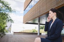 Mujer de negocios sentada fuera del edificio de oficinas y hablando por teléfono móvil - foto de stock