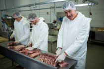 Macellai sorridenti che tagliano carne in fabbrica di carne — Foto stock