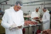 Boucher mâle tenant des dossiers sur presse-papiers à l'usine de viande — Photo de stock