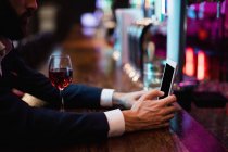 Empresário usando telefone celular com copo de vinho no balcão no bar — Fotografia de Stock