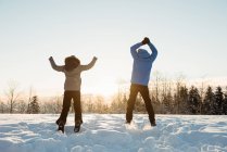 Rückansicht eines Paares, das auf verschneite Landschaft springt — Stockfoto