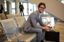 Бизнесмен с паспортом, посадочным талоном и портфелем сидит в зале ожидания терминала аэропорта — стоковое фото