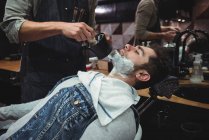 Milieu de section de barbier appliquer de la crème sur la barbe du client dans le salon de coiffure — Photo de stock