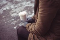Close-up de mulher segurando copo de café descartável na margem do rio no inverno — Fotografia de Stock