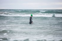 Visão traseira do atleta em terno molhado em pé no mar — Fotografia de Stock