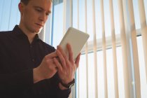 Чоловічий керівник використовує цифровий планшет біля віконних жалюзі в офісі — стокове фото