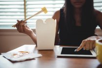 Женщина, использующая цифровой планшет во время еды с палочками для еды дома — стоковое фото