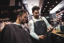 Barbier montrant coiffure au client sur tablette numérique dans le salon de coiffure — Photo de stock