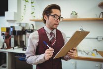 Man writing with pen on clipboard in coffee shop — Stock Photo