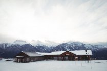 Casas no campo coberto de neve por montanhas contra céu nublado — Fotografia de Stock