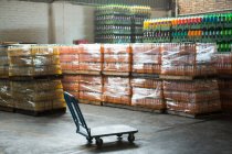 Chariot vide et bouteilles de jus emballées disposées en entrepôt — Photo de stock