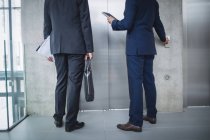 Baixa seção de empresários em pé por elevador e pressionando o botão no escritório — Fotografia de Stock