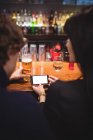 Casal usando telefone celular no balcão de bar — Fotografia de Stock