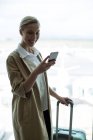 Femme d'affaires avec bagages utilisant un téléphone portable à l'aéroport — Photo de stock