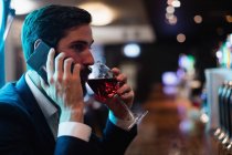 Businessman talking on mobile phone while having glass of wine in bar — Stock Photo