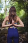 Вид ззаду жінки, що виконує йогу в лісі в сонячний день — стокове фото