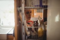 Mulher bonita olhando prateleiras na cozinha em casa — Fotografia de Stock