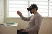 Вид сбоку человека, использующего гарнитуру виртуальной реальности, сидя за рабочим столом — стоковое фото