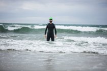 Спортсмен в мокром костюме стоит в море на пляже — стоковое фото