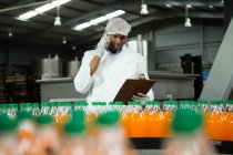 Trabalhador do sexo masculino falando por telefone enquanto examina produtos na fábrica — Fotografia de Stock