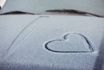 Gros plan de la forme du cœur dessiné sur le capot de voiture recouvert de neige — Photo de stock